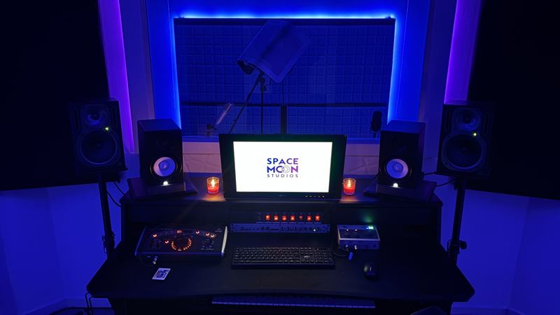 Sala principal de Space Moon Studios: monitores de estudio, micrófono con filtro antipop y paneles acústicos con iluminación LED azul